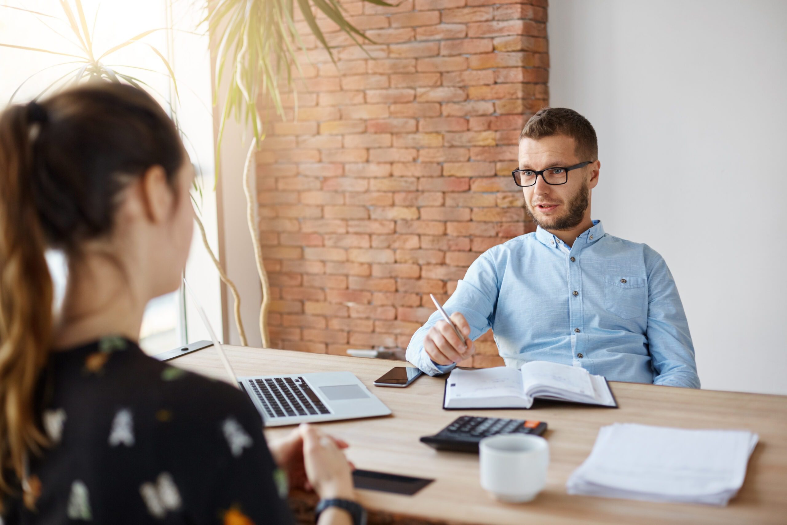 Close up of mature bearded company director in glasses sitting in office with dark-haired girl in front of him on job interview. Man asking women about work experience